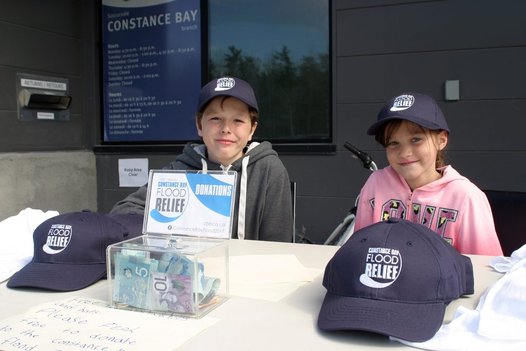 From left, Levon Lucente, 10, and Kaylee Plourde, 9, raise money and give away swag at the sandbagging operation at the NorthWind Wireless Fiber Centre today. Photo by Jake Davies﻿