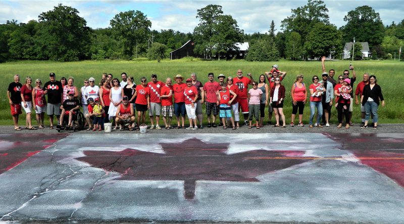 The Borgs' annual Canada Day party people pose behind the massive Canada Day flag they painted on the Carp Road June 30. Courtesy Ken Borg