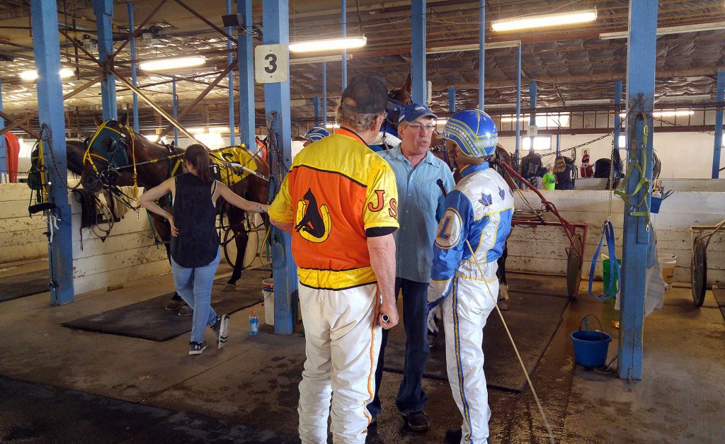 Wayne Laviolette talks with trainer John Smith, left, and driver 
Rodney LaFramboise in the stables before post time. Photo by Jake Davies