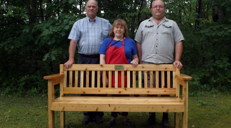 From left, Ches Booth, market manager Cindy Pratt and memorial builder and marker vendor Chris Kritsch pose with the memorial bench in honour of Judy Booth. Photo by Jake Davies