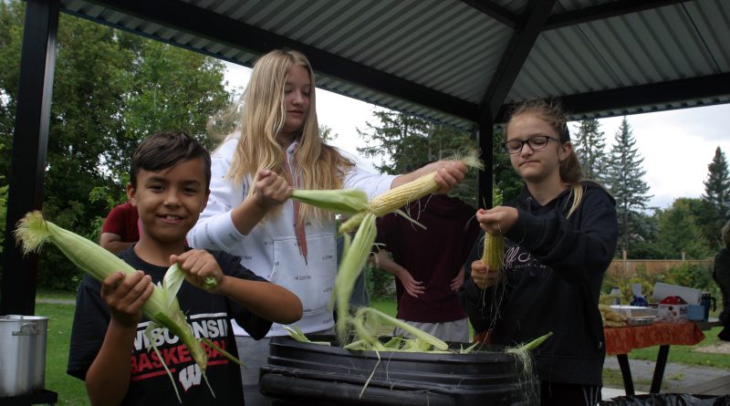 From left, young volunteers Kristjan Chute, 10, Zoe Riches, 12, and sister Lola Riches, 10, husk some corn at the Marathon Village Corn Roast last Saturday. Photo by Jake Davies