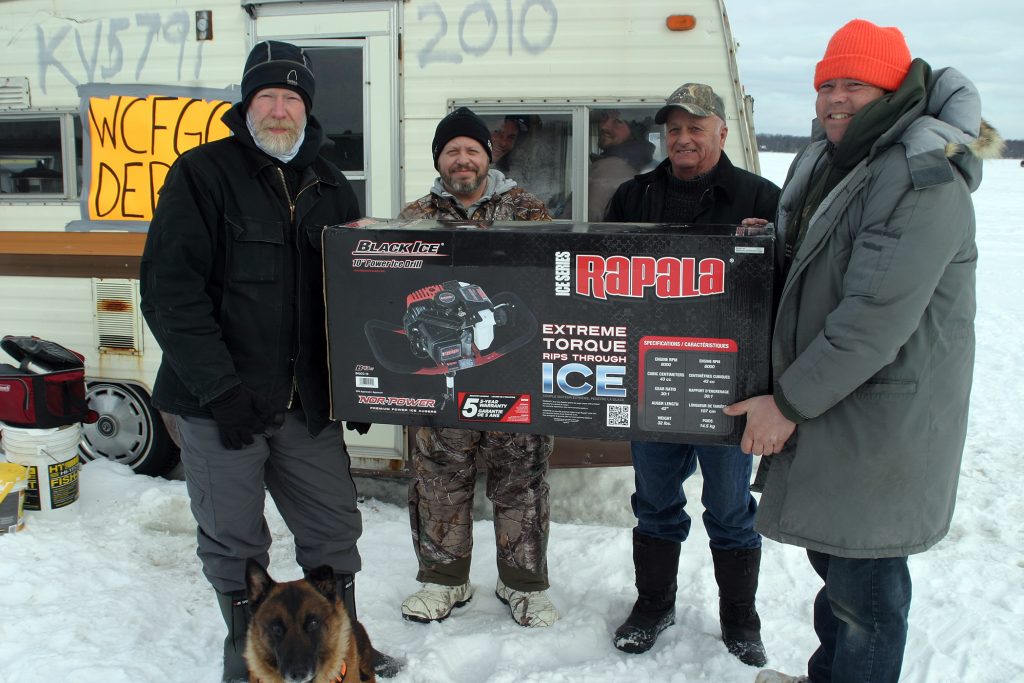 From left, WCFGC board members Warren Backler, Brent Boyd, Wilson Boyd and Adam Boyd pose with the top prize while a couple of anglers photobomb from the comfort of the fish shack. Photo by Jake Davies