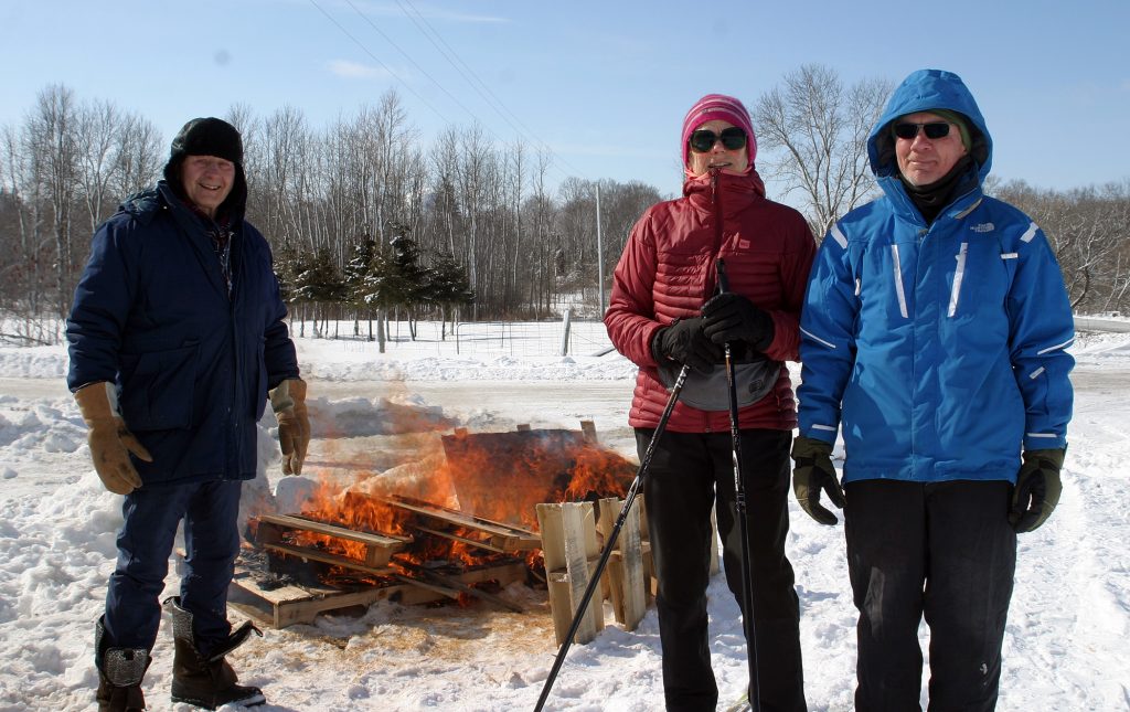 From left, volunteers George Wilson, Béatrice Romeskie and Dan Kovacs keep the fire burning along the cross-country ski trail. Photo by Jake Davies