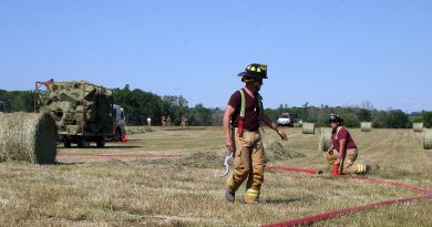 A firefighter stands in a hay field.
