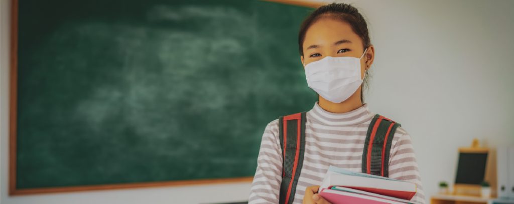 A young student in school wears a mask.