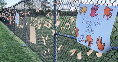 A photo of a fence with signs and orange ribbons on it.