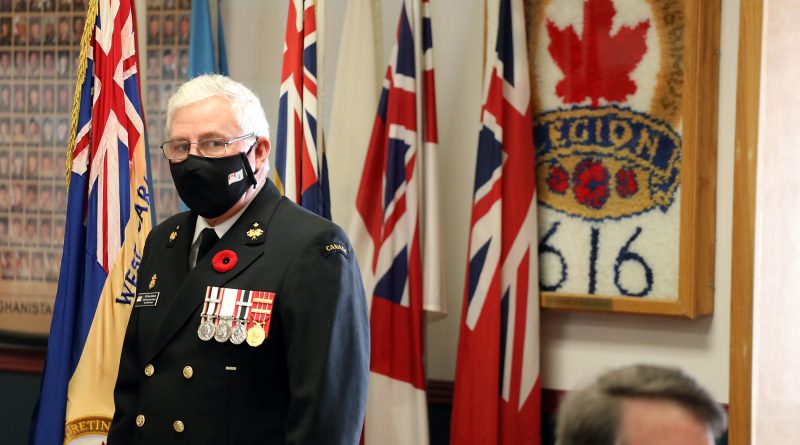 A Legion member stands in front of the Branch insignia.