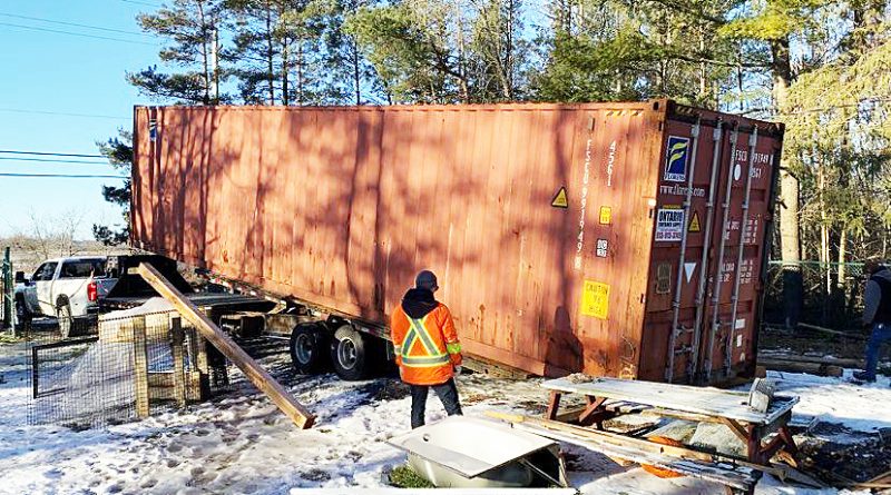 A photo of a shipping container being unloaded off a trailer.