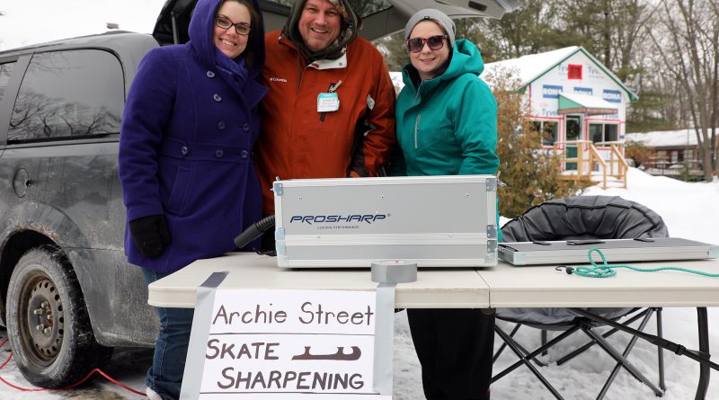A photo of three volunteers and the skate sharpening machine.