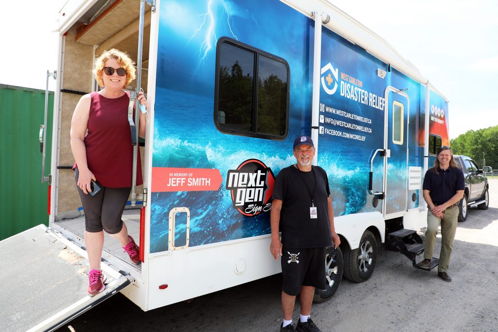 A photo of three people standing in front of a trailer.