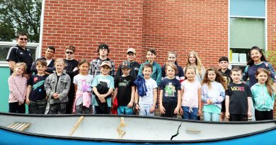 A photo of school kids posing in front of a canoe.