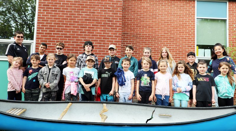 A photo of school kids posing in front of a canoe.