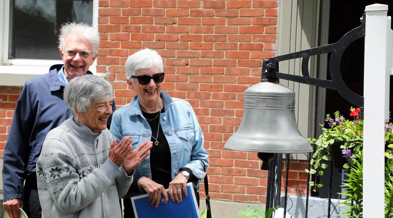 Three people admire a school bell.