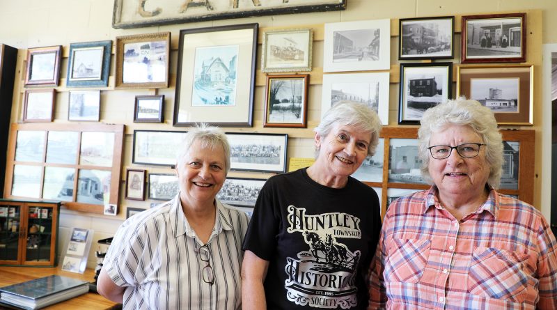 A photo of three ladies standing in front of old photos.