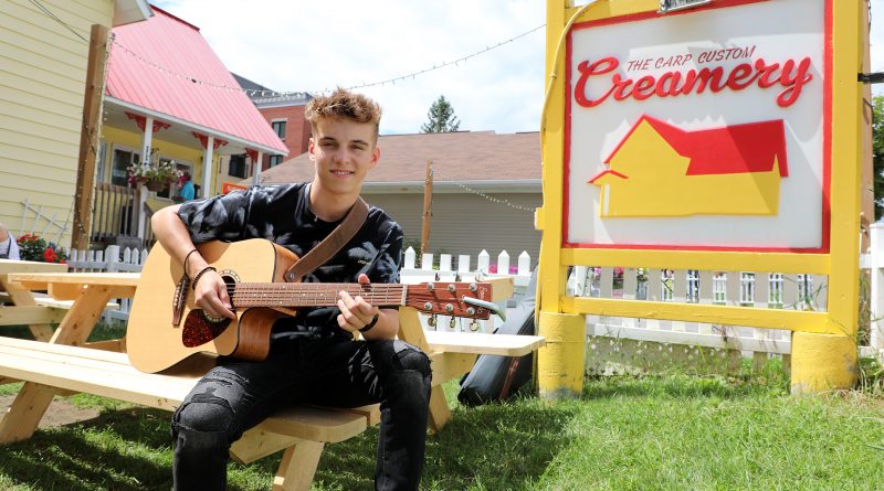 A photo of Carson with his guitar in front of the Carp Creamery.