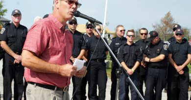 A photo of a man speaking with a line of firefighters behind him.