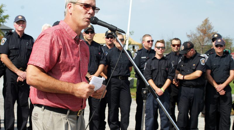 A photo of a man speaking with a line of firefighters behind him.