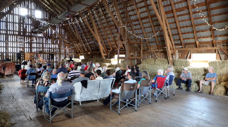 A photo of a group of people seated in a barn.