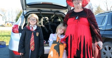 Three costumed people pose in front of the trunk of a car.