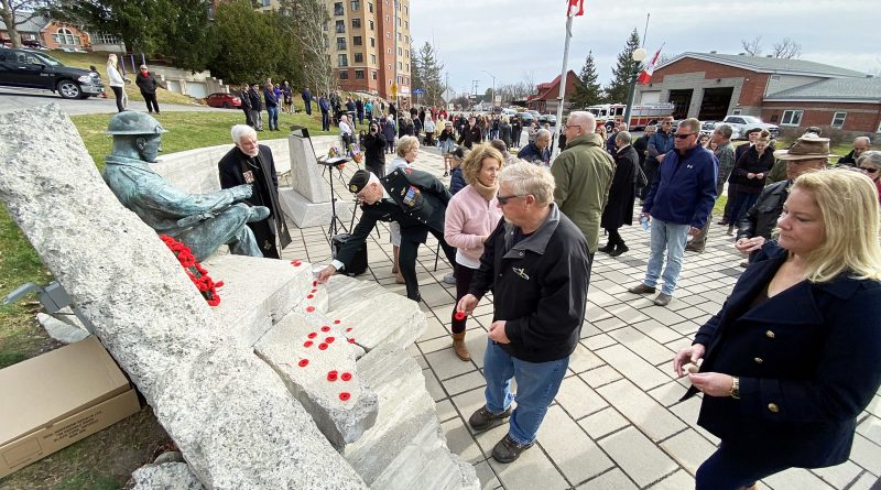 A photo of people laying their poppies on a war memorial.