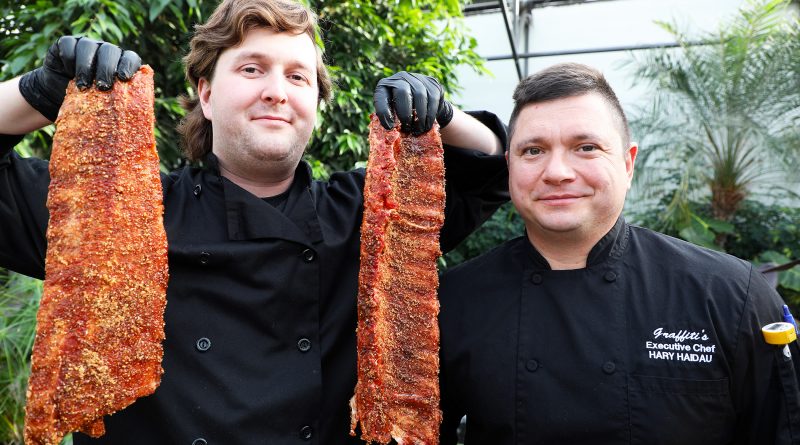 A photo of two chefs holding giant baby back ribs.
