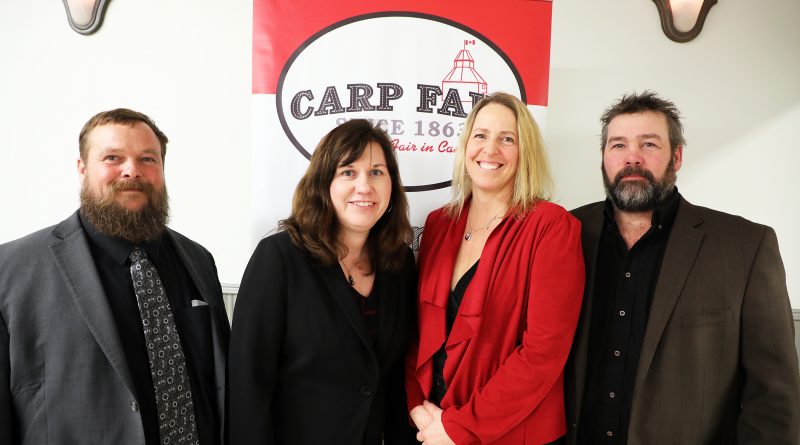 Four people pose in front of a Carp Fair banner.