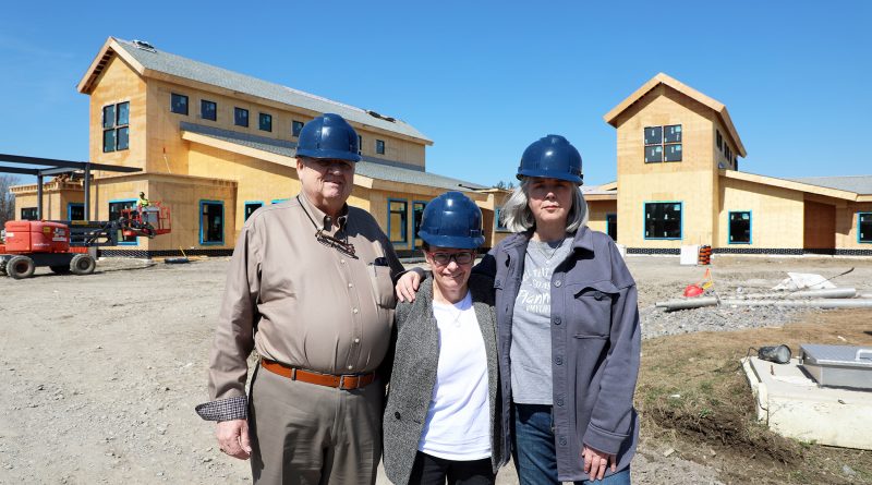 Three people stand in front of a building under construction.