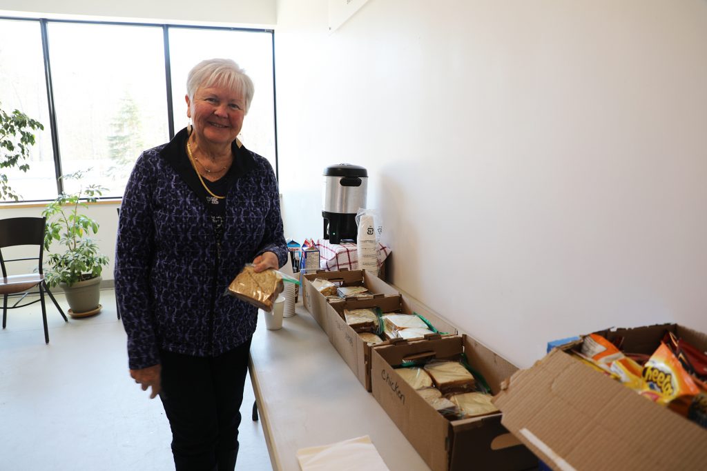 A woman stands beside some food.