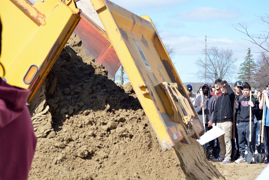 A dumptruck dumps sand while WCSS students look on.