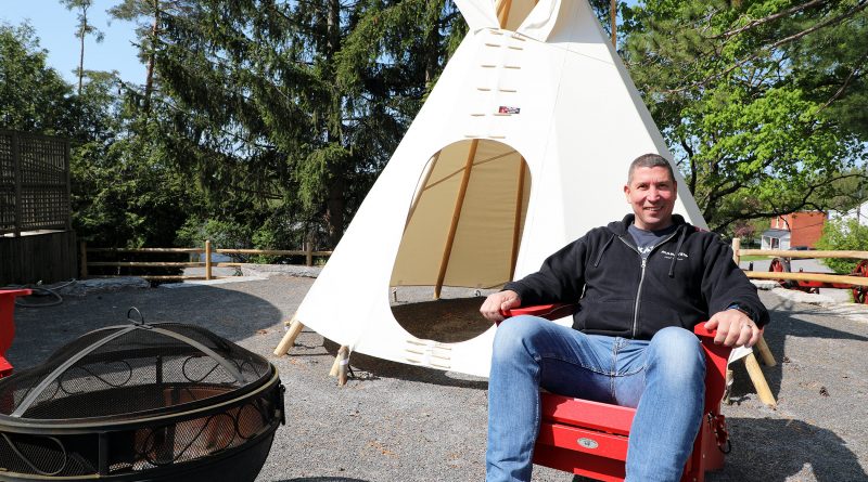 A man sits in front of a tipi.