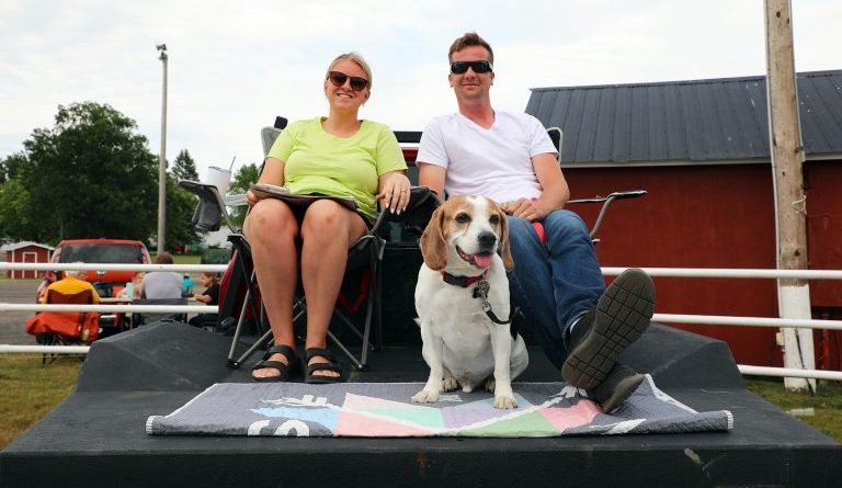 Two people and a dog sit on the back of their vehicle playing bingo.