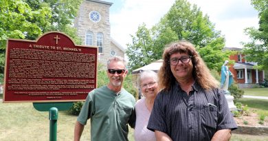 Three people stand beside a historical plaque for St. Michael's Corkery.