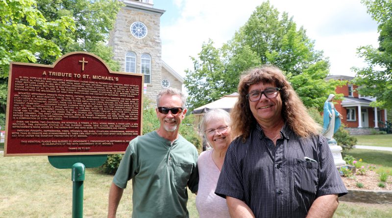 Three people stand beside a historical plaque for St. Michael's Corkery.