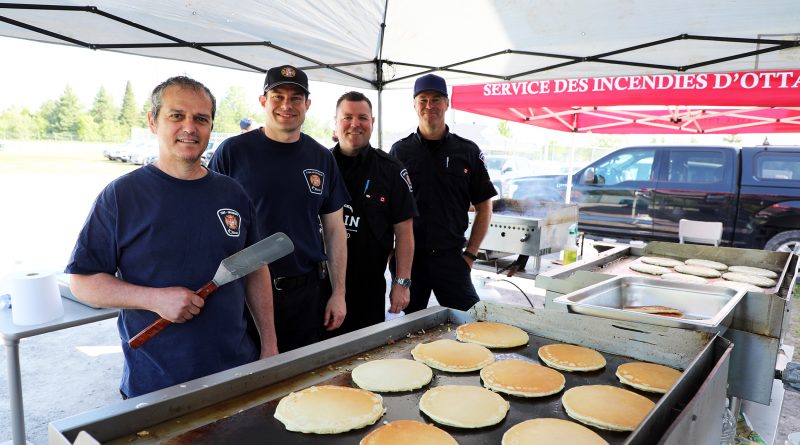 Four firefighters pose beside a stack of pancakes.