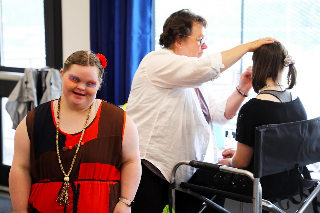 A model poses for a photo while another gets their face painted.