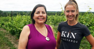 Two people pose in a vineyard.