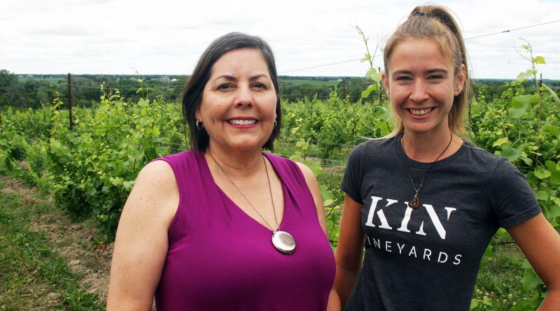 Two people pose in a vineyard.