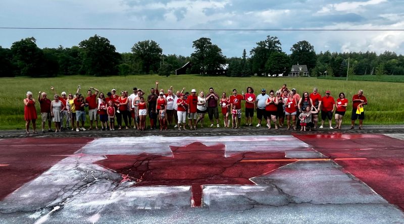 People pose around a Canada Day flag painted on a road.