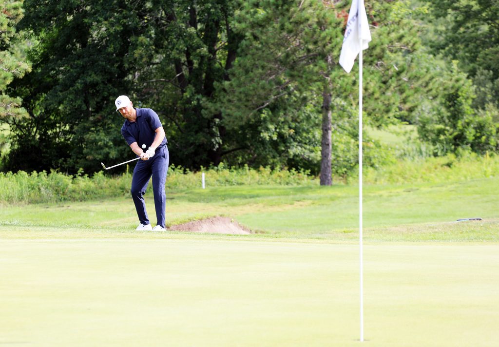 A hockey player chips a golf shot.