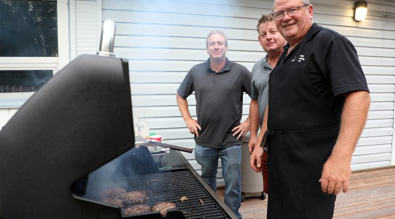 Three men pose at a barbecue.