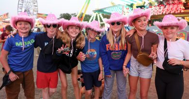 A group of seven people pose in pink cowboy hats.
