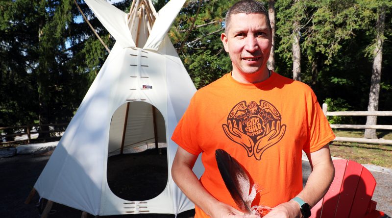 A man stands in front of a tipi.