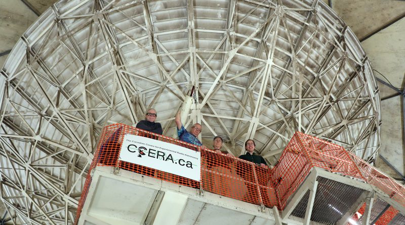 Four men pose under a huge antenna.