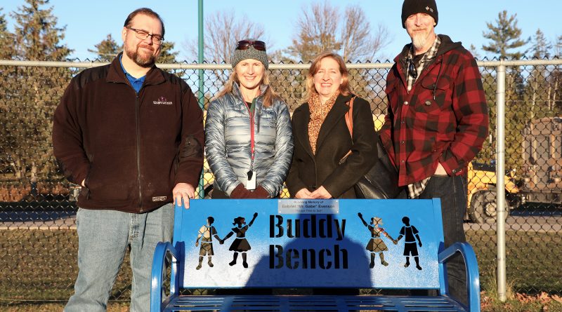 Four people pose behind a bench.