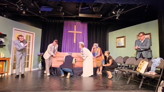 Actors perform on a stage around a casket,