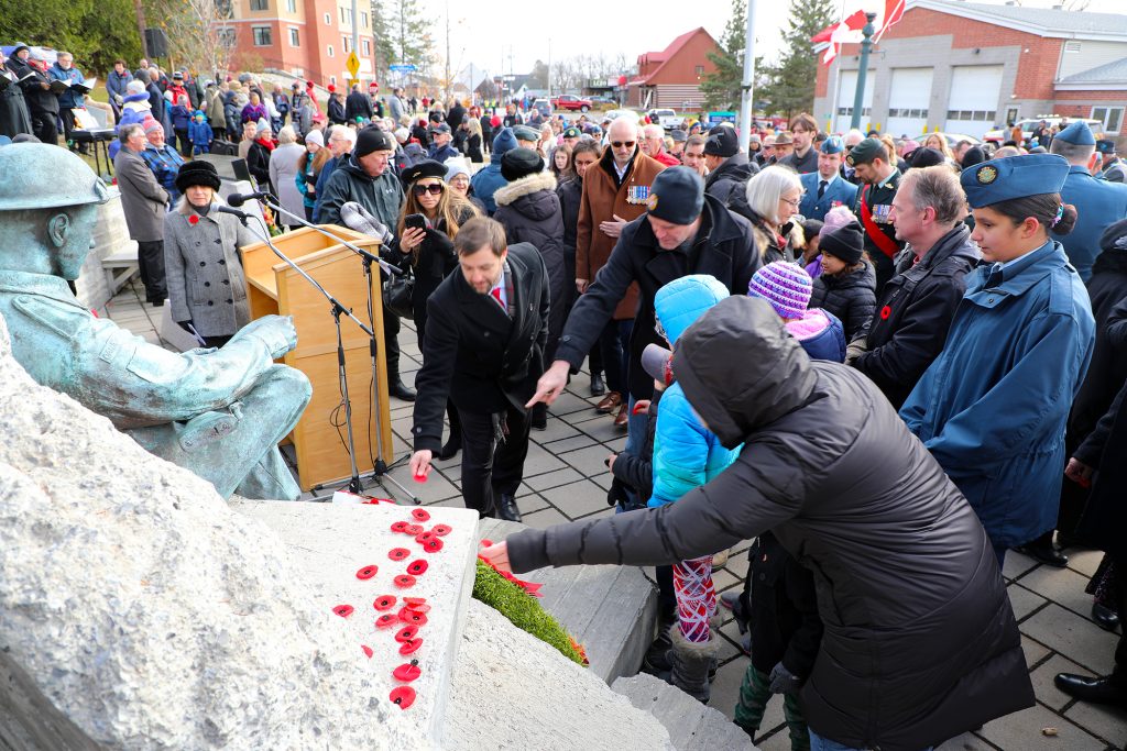 A man places a poppy on a statue.