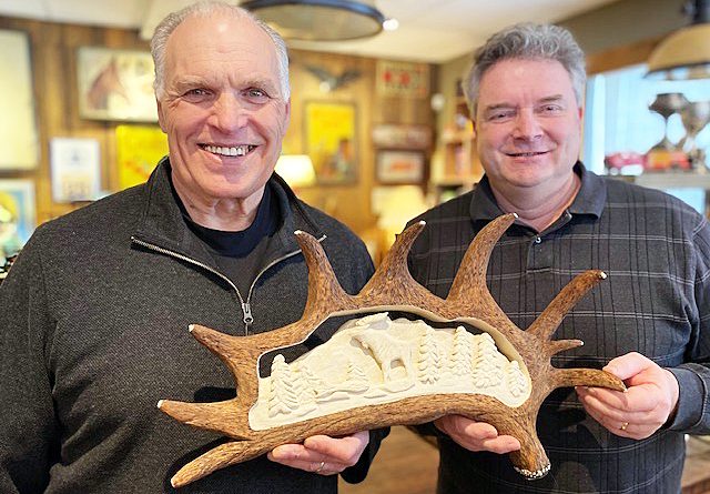 Two men pose with a carving.
