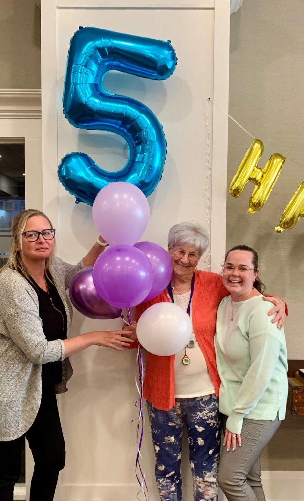 Three people pose with balloons and the number five.
