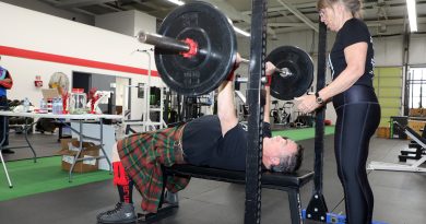 A person performs a bench press with a spotter nearby.