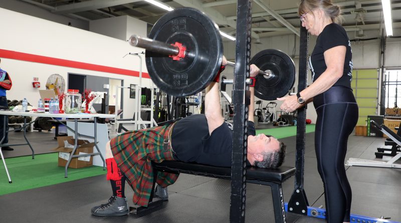 A person performs a bench press with a spotter nearby.
